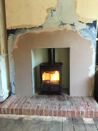 Wood-burning stove with a glowing fire, set in an unfinished wall with plaster.